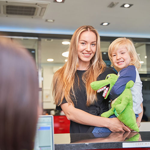 Smiling mum holding toddler at general practice reception desk